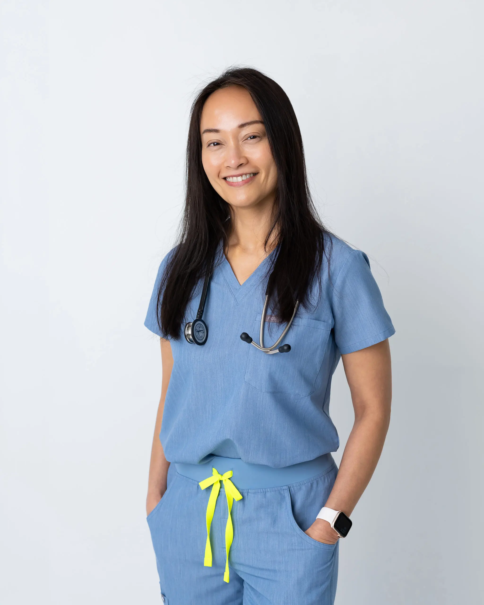 Smiling female healthcare professional in blue scrubs with stethoscope.
